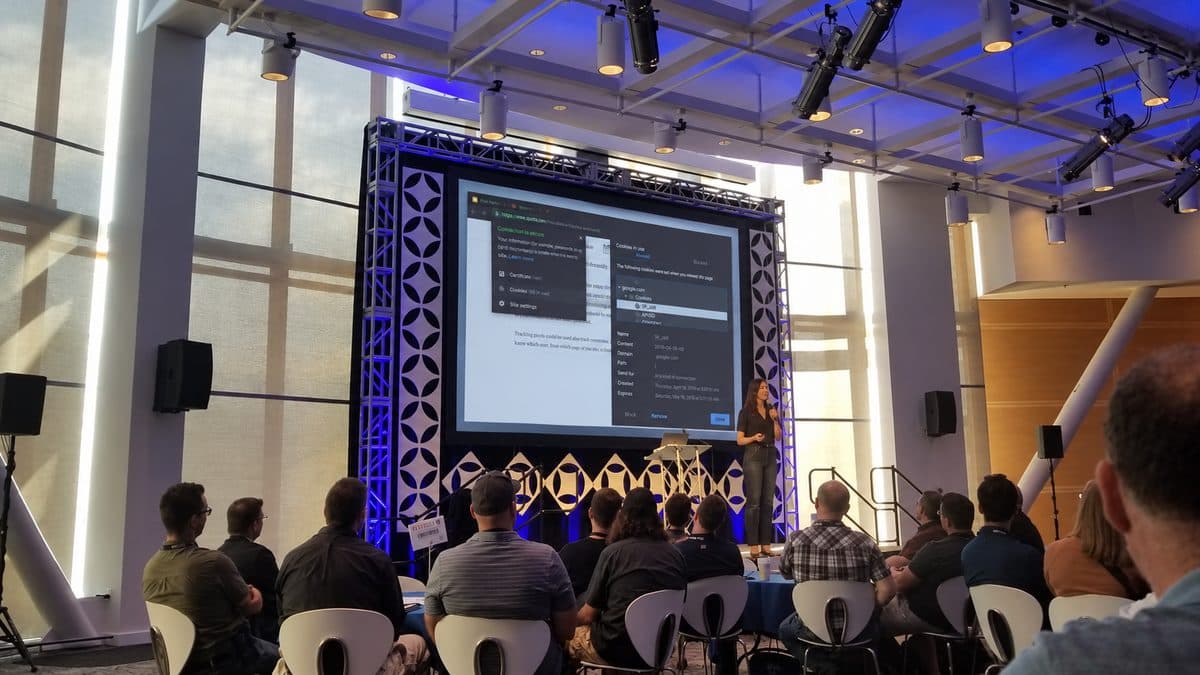 Kelsey on stage at DevOpsDays Boise in 2019, presenting a browser's cookie inspector on a large screen to a seated audience