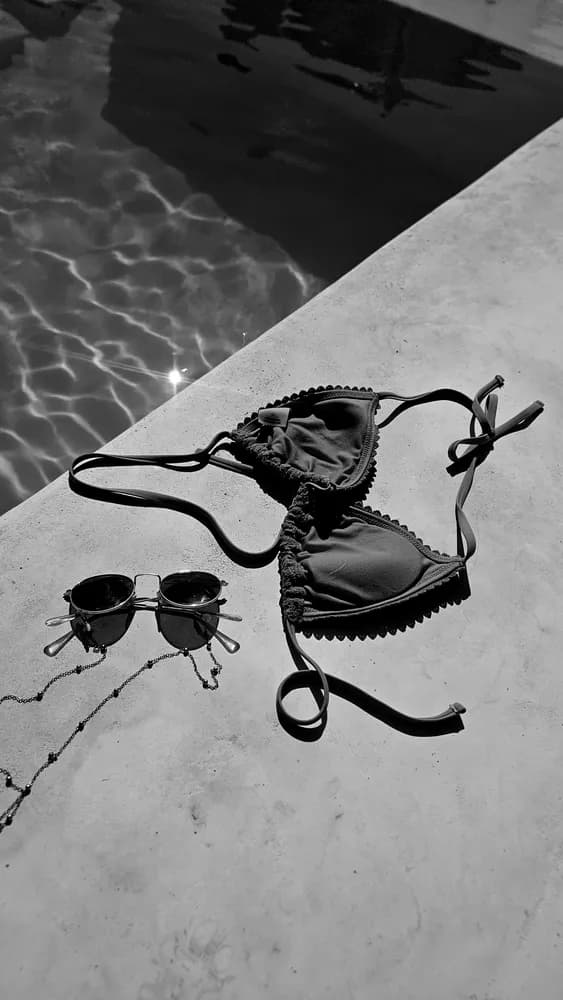 Black-and-white flat lay of a bikini top and sunglasses on a pool deck