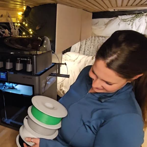Kelsey holding filament spools beside a 3D printer in her van