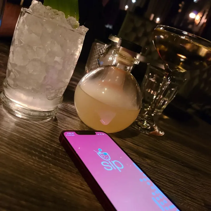 The Sip app open on a phone beside cocktails on a bar table