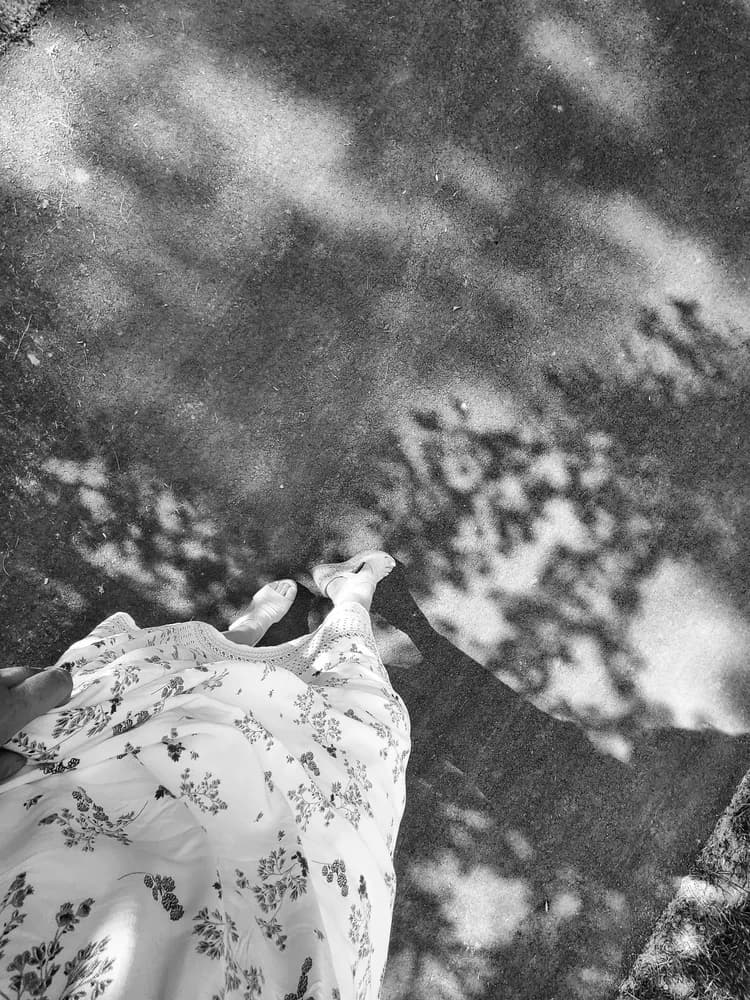Black-and-white overhead shot of a floral dress and sandals on a sun-dappled path