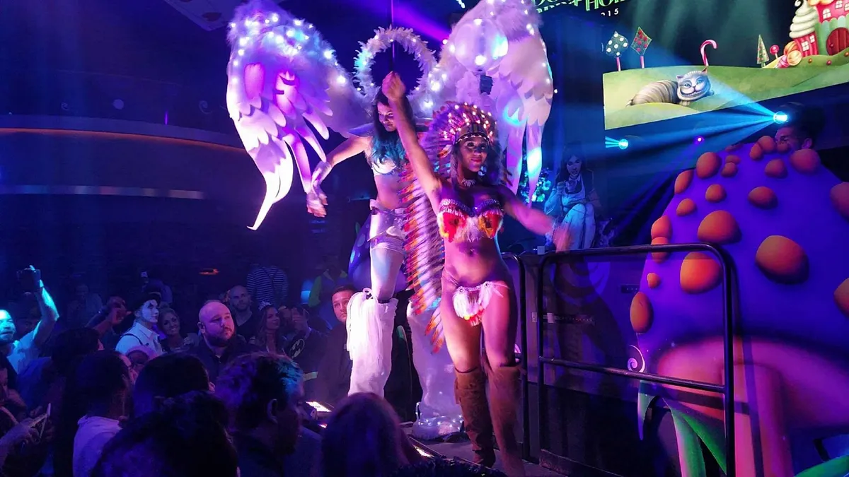 A stilt performer with lit white wings on a nightclub stage
