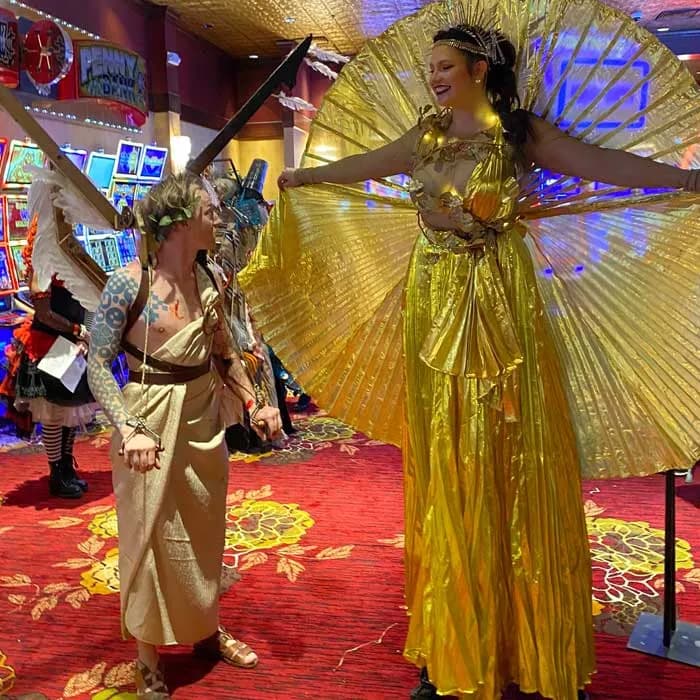 A stilt performer in a gold gown with pleated wings spread wide