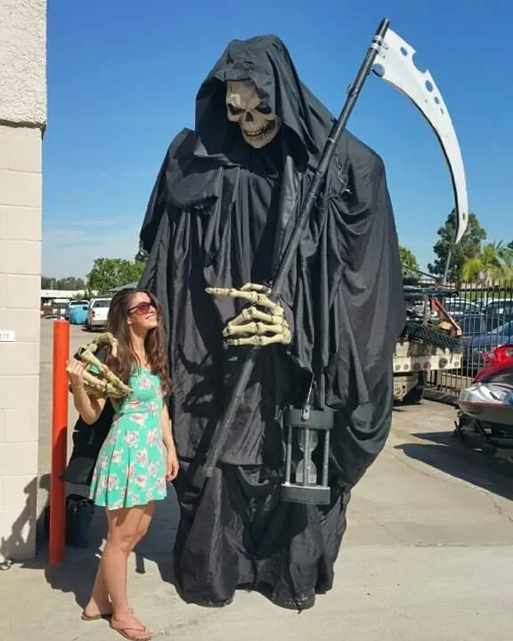 A giant grim reaper puppet beside a woman in a floral dress